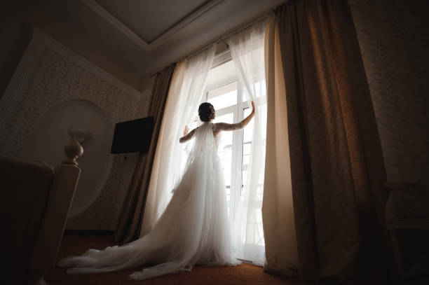 istock bride in a white dress with a plume opens the curtains 944130286