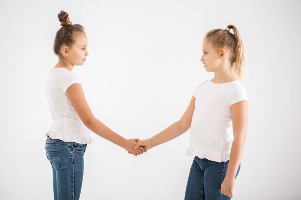 Blonde girls shaking hands after quarrel against white background