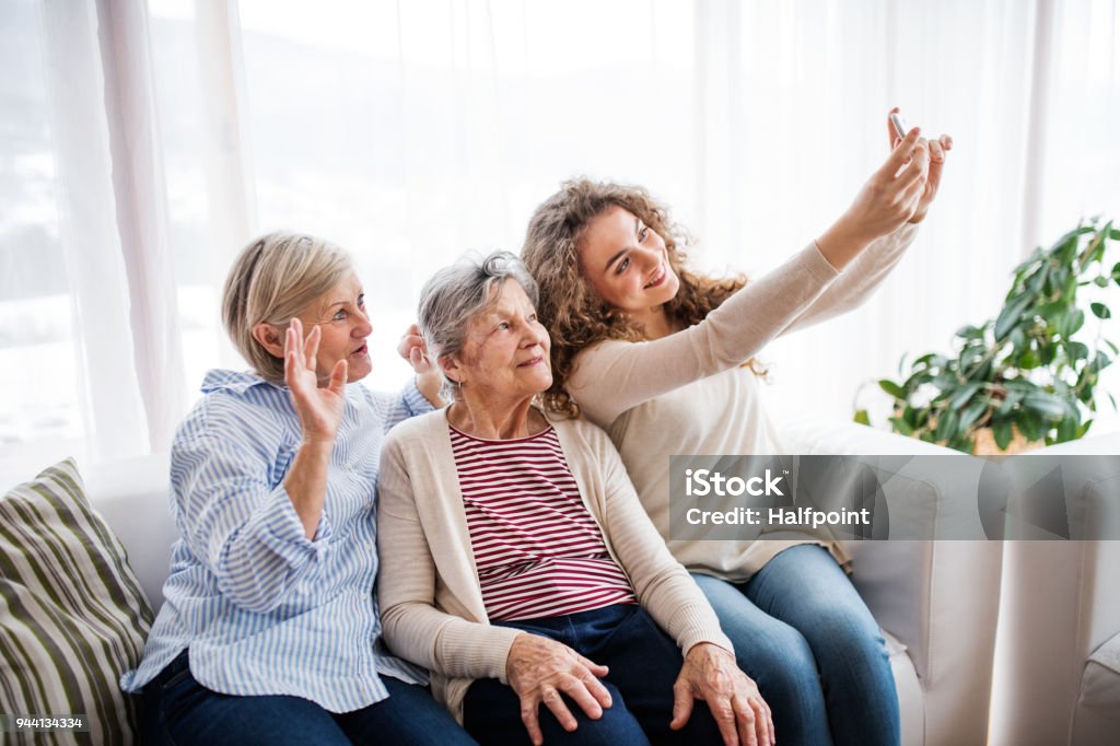 A teenage girl, mother and grandmother with smartphone at home. A teenage girl, her mother and grandmother with smartphone at home, taking selfie. Family and generations concept. Multi-Generation Family Stock Photo