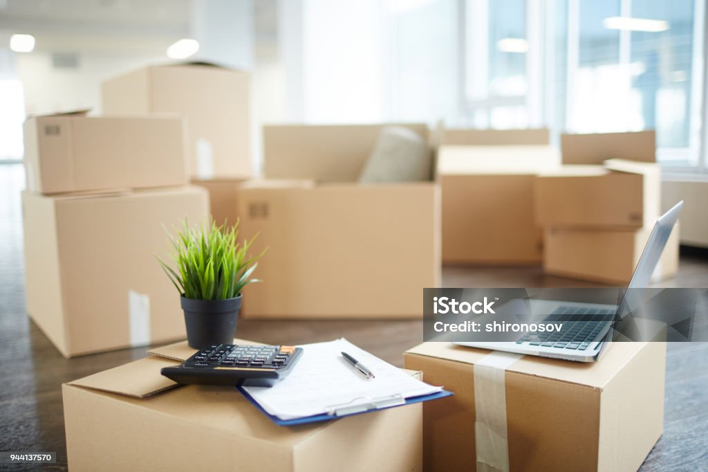 Accountant supplies Several unpacked carton boxes with office supplies, laptop, papers, calculator and green plant in flowerpot on top of packages Relocation Stock Photo