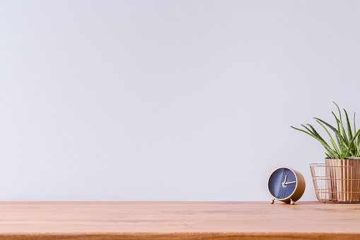 Photo of wooden home office desk with black and gold clock and fresh green plant and white empty wall