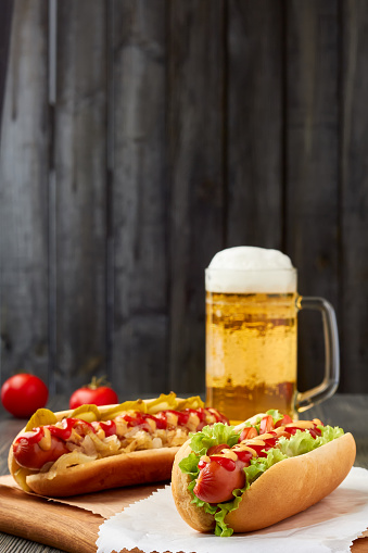 Two hot dogs and mug of beer on wooden background. Copy space