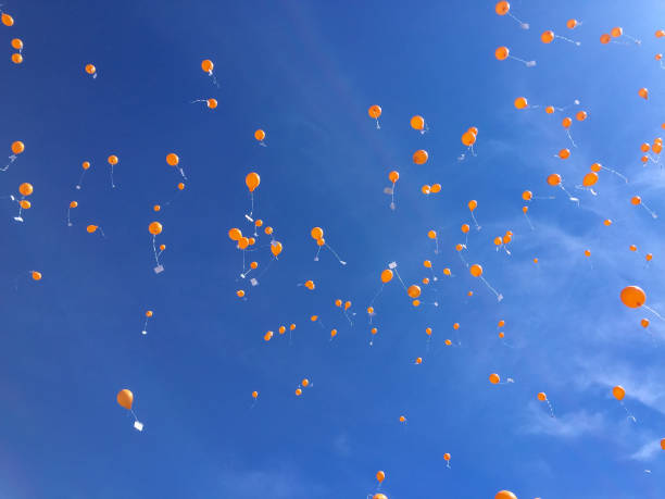 A blue sky background and some orange balloons flying away. Typical dutch tradition on King's day