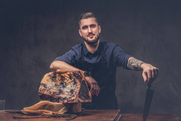 Professional butcher holds a knife standing with raw smoked meat stock photo