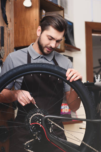 istock young worker in apron holding bicycle wheel and fixing chain in workshop 944193248