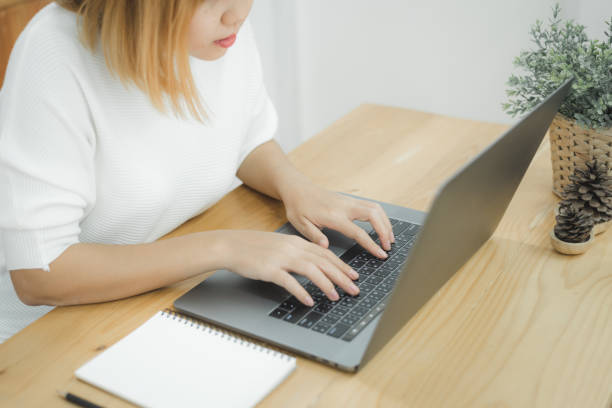 istock Beautiful young smiling Asian woman working on laptop while at home in office work space. Businesswoman working from home via portable computer writing on keyboard. Enjoying time at home. 944195156