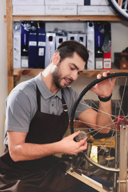 istock smiling young man in apron fixing bicycle wheel in workshop 944203196