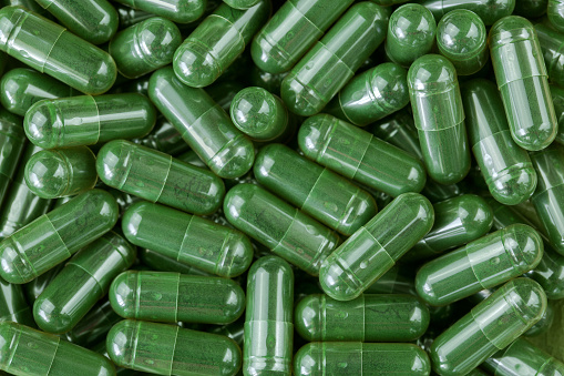 Green Spirulina powder, blue-green algae in clear capsules as dietary supplement