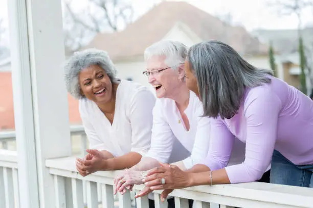 Photo of Three senior female friends laugh together on front porch