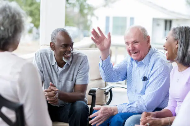 Photo of Senior man shares joke with friends on front porch