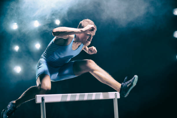 hurdling male athlete in the middle of the jump - hurdling hurdle running track event imagens e fotografias de stock