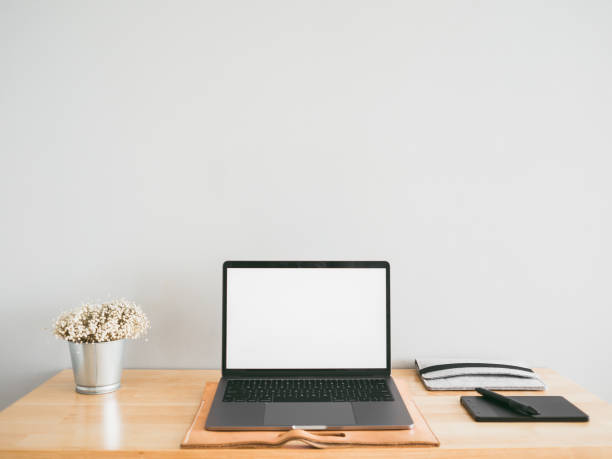 istock Laptop and some stationary tools on wooden work desk with empty gray wall as background. Concept of workspace and minimal office. 944251638