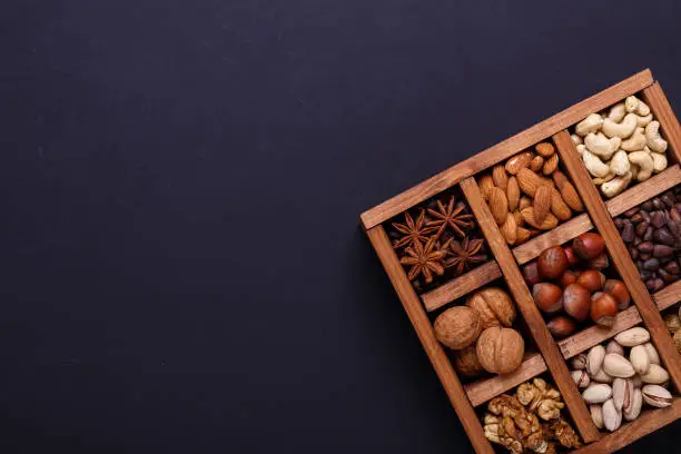 Assortment of nuts in a wooden box on a black background - healthy snack. Top view. Copy space