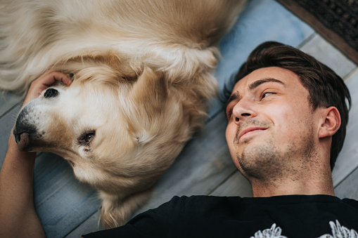 High angle view of smiling man enjoying while lying next to his dog on the floor.