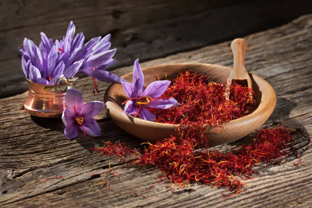 Photo of Saffron in wooden bowl on wooden table with saffron flowers on the side