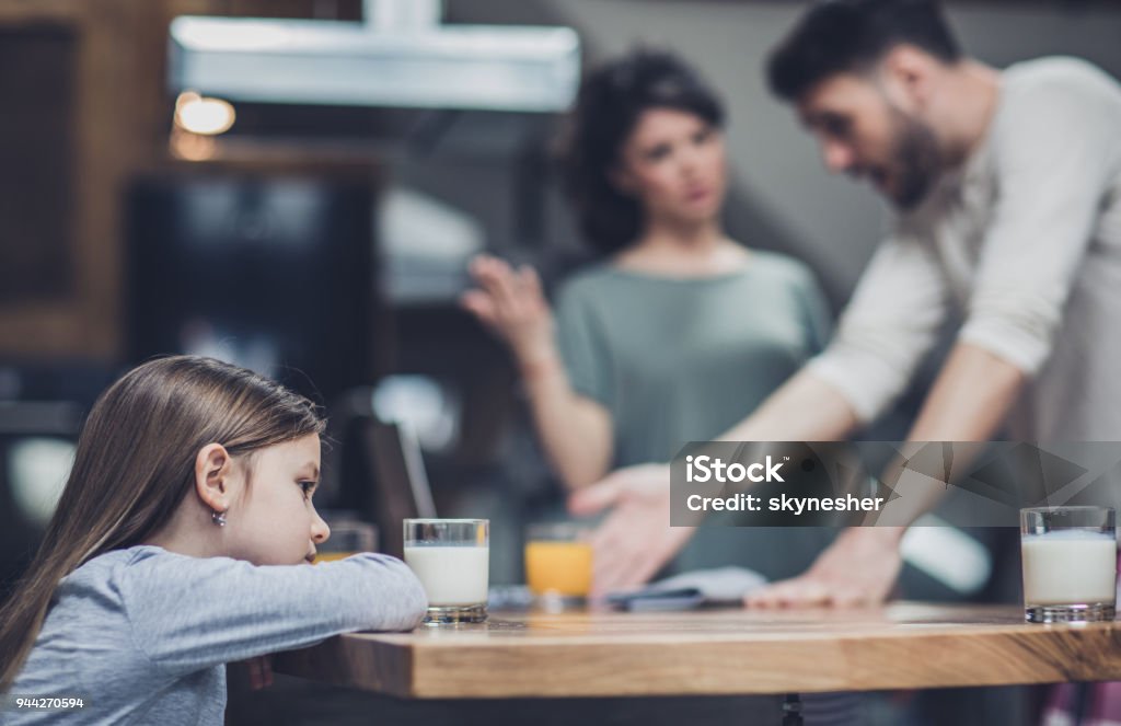 Why are they arguing? Little girl feeling sad while her parents are arguing in the background. Parent Stock Photo