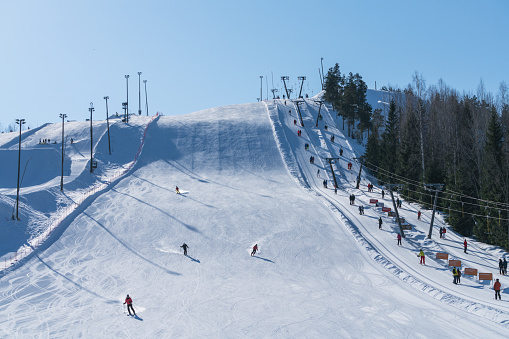 Himos, Finland – April 1, 2018: Ski slope and ski lift in Himos in the sunny winter morning with clear blue sky. Four skiers are going down the slope.