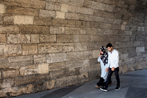 Young muslim couple walk hand in hand in front of old, stone wall in Eminonu /Sirkeci area of Istanbul.