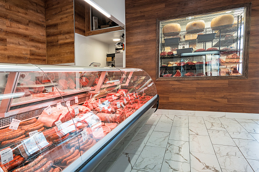 Display refrigerator with meat products and a walk in refrigerator with cheese and aged meat in a grocery delicatessen store.