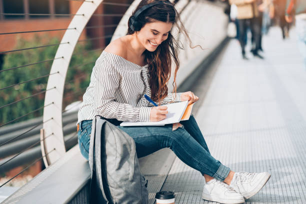 istock Student with headphones writing homework outdoors 944300658