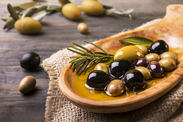 mixed olives with rosemary in the foreground wooden bowl in the foreground with rosemary olives and virgin oil on the wooden table olive fruit stock pictures, royalty-free photos & images