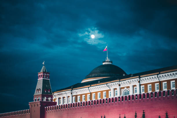 Kremlin Moscow Dome of Senate and red wall Night shot of the Kremlin Moscow Dome of Senate building, a red Kremlin wall, flag of Russia with the emblem on it; overcast dark-blue sky with a bright moon kremlin stock pictures, royalty-free photos & images