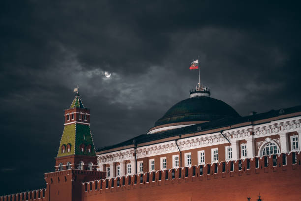 Dark night shot of Russian Kremlin: Senate dome, tower, wall Night shot: Kremlin Moscow Dome of Senate building, a red Kremlin wall, flag of Russia with the emblem on it; sinister dark sky with a moon partly closed by the clouds kremlin stock pictures, royalty-free photos & images