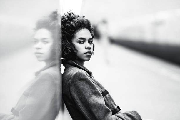 Greyscale portrait of black girl at the metro station Black and white portrait of charming African American female in the coat leaning against a mirror wall; the greyscale shot of a cute black teenage girl sitting on the bench of an underground station train station black and white stock pictures, royalty-free photos & images