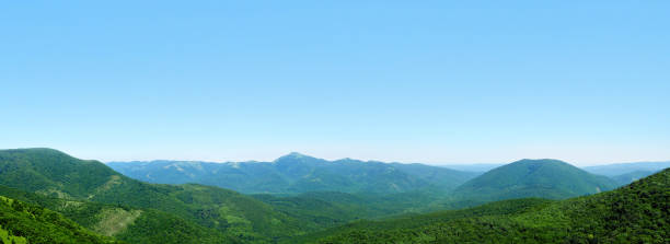 Beautiful panoramic mountain landscape, low hills and mountain peaks covered with green forest, blue sky. Skyline, Markhotsky Range, Russia