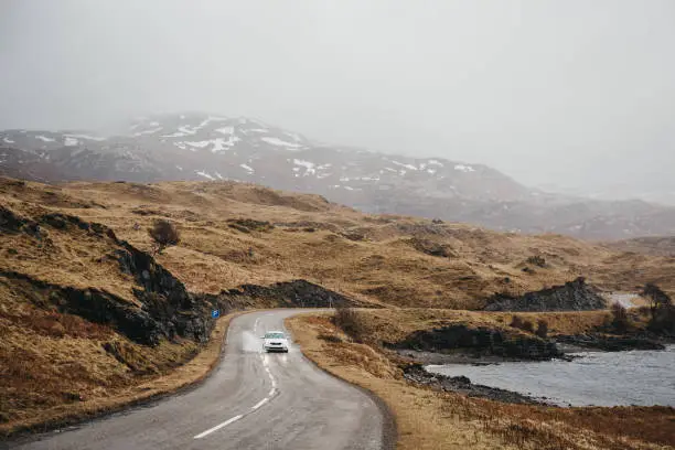 Unidentified car driving on a road going through Scottish Highlands near Lochinver on a foggy spring day.