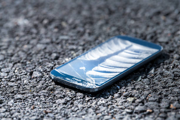 istock Asphalt pavement road with broken phone smartphone, cracked screen fell on ground 944319448