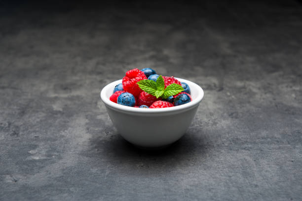 Berry fruit in white ceramic bowl on dark concrete background.