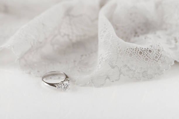 istock White gold wedding ring with diamonds on white background with lace 944332948