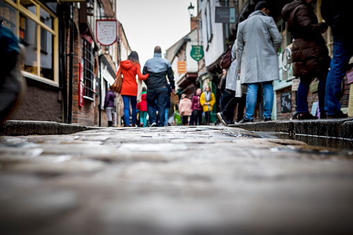Low down shot of people and couple walking holding hands down a old traditional cobbled English street whilst browsing in shops on retail therapy day in the UK