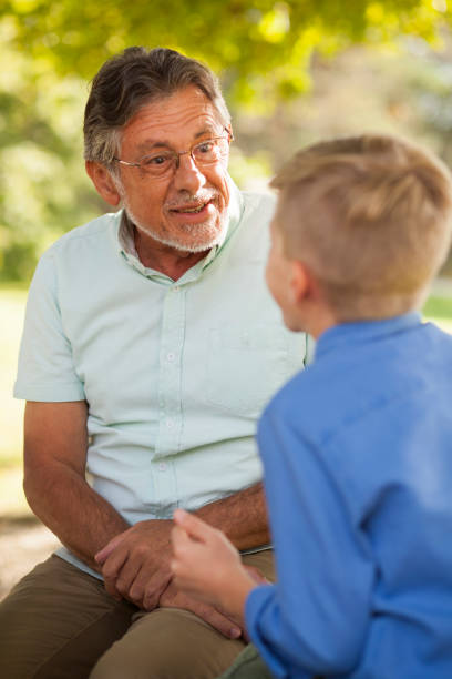 Grandson telling stories to his granddad Senior man surprised at his grandson's stories. Sitting on bench in nature. teacher retirement party stock pictures, royalty-free photos & images