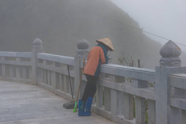 SaPa, Vietnam - August 20, 2017: Cleaner, worker in traditional Vietnamese hat browsing her phone