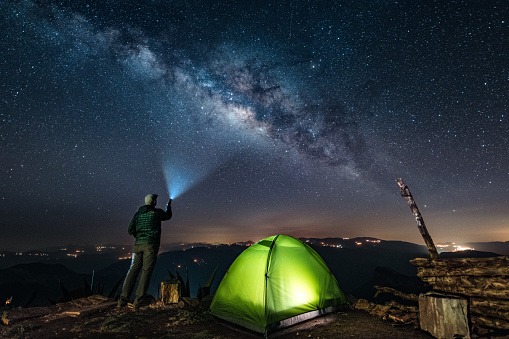 Solo traveler standing by camping tent looks at the milky way at Sierra Gorda of Queretaro, Mexico.