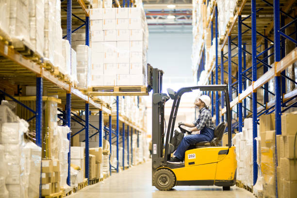 Warehouse driver operating forklift Serious busy young warehouse driver operating forklift to put heavy packaged boxes on shelf forklift truck stock pictures, royalty-free photos & images
