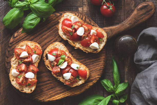 antipasti italiano bruschetta con tomate, queso mozzarella y albahaca sobre tablero de madera - brushetta fotografías e imágenes de stock