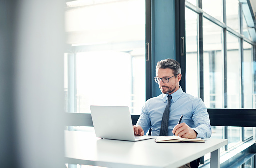 Shot of a mature businessman using a laptop at his desk in a modern office