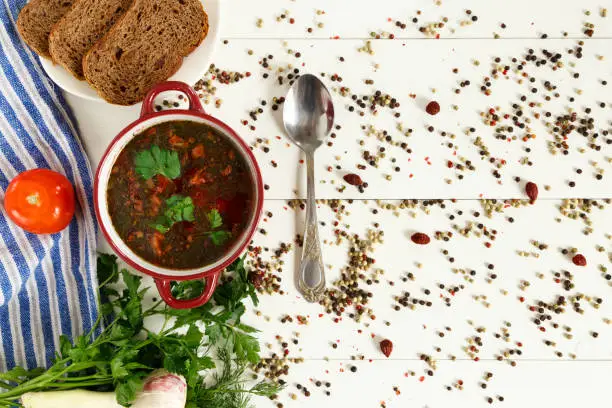 Ukrainian and Russian traditional soup borsch. Black bread, parsley, fennel and tomatoes with spices. White wooden table. Top view. Copy space