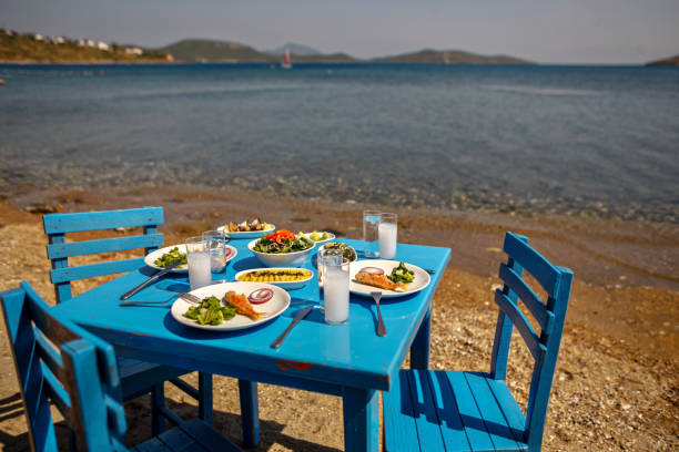 aperitivos e raki ou ouzo servido numa mesa azul na praia além de belíssima vista mar - greek culture bar restaurant greece - fotografias e filmes do acervo