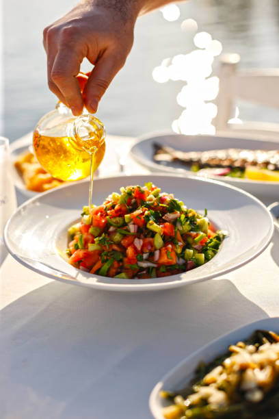 waiter mâle, verser l’huile d’olive, vinaigrette sur la salade méditerranéenne - mediterranean diet photos et images de collection