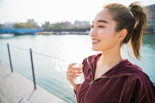 Japanese young woman drinking cold water at riverside park