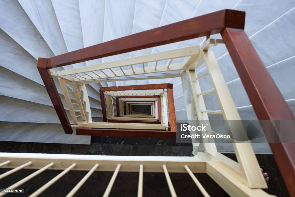 View down to spiral stairway with marble steps, wooden rails Perspective view down to spiral geometrical stairway of marble steps and wooden rails Aperture Stock Photo