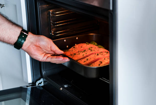 istock Man putting raw salmon steak into oven 944490782
