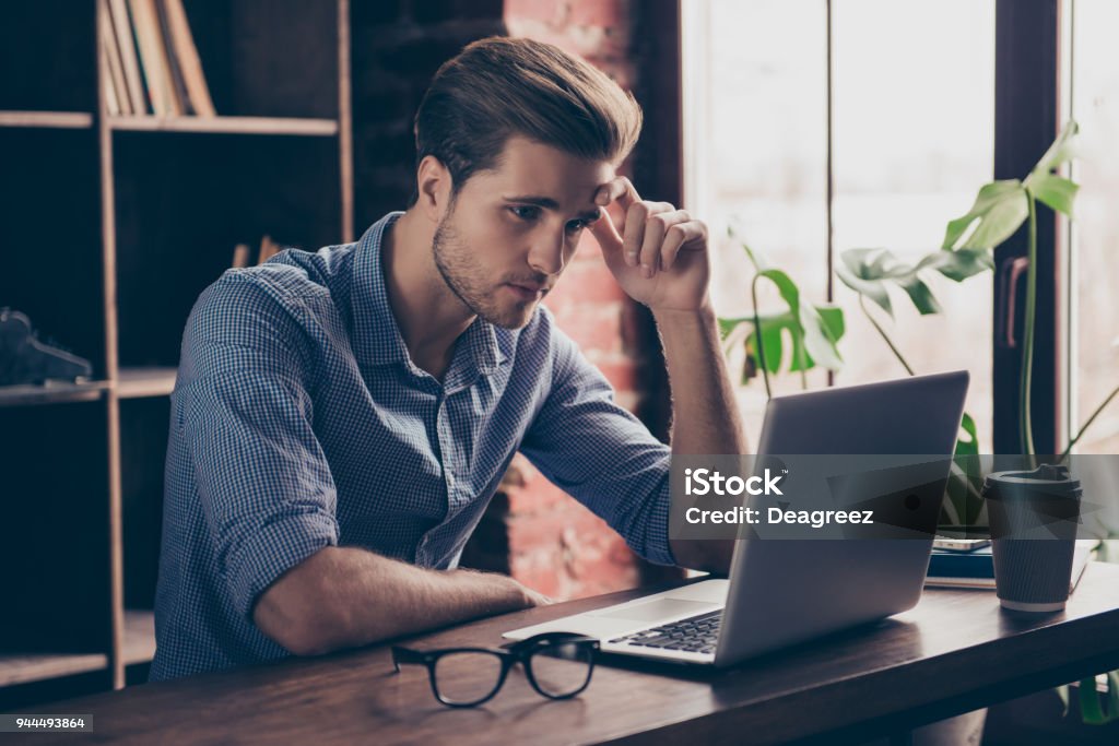 Young manager in checkered shirt reading information on the Internet on his computer Concentration Stock Photo