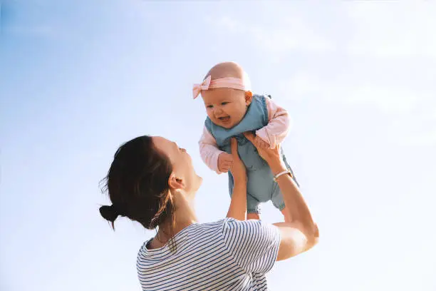 Young mother throws up baby in the sky, summer outdoors. Happy mom and cute smiling baby girl. Positive human emotions, feelings, natural lifestyles. Family background.