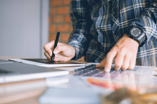 Freelance creative designers working on desk using digital graphic tablet and drawing with pen in modern home office.