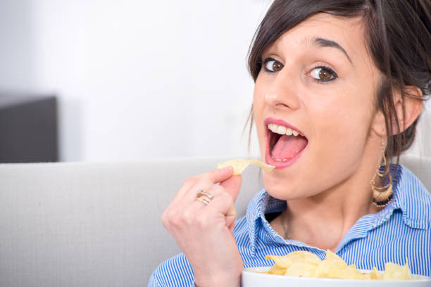istock pretty young brunette woman eating chips 944516126